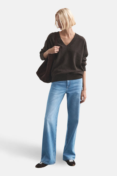 Jean droit bleu clair de MANGO, porté avec un pull marron et une veste sur épaules.