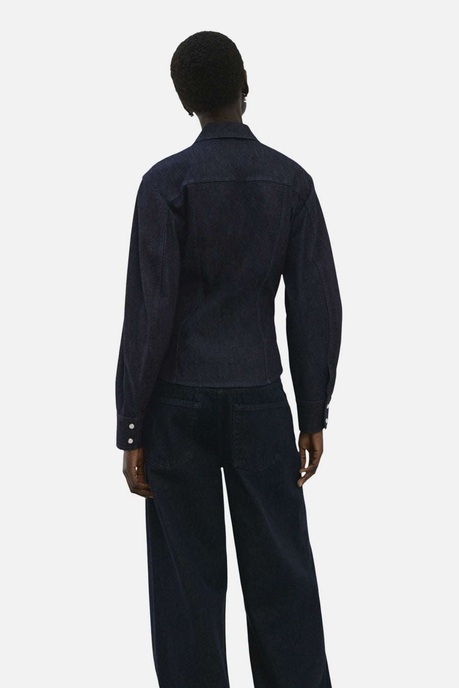 Donkerblauw denim overhemd met lange mouwen van MANGO, gezien van achteren met rechte, donkere jeans.
