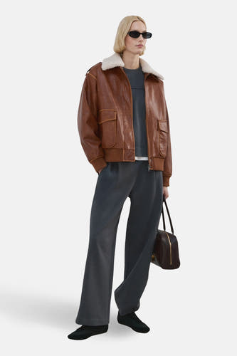 Jean de jogging bleu de MANGO, avec des jambes larges et porté avec une veste en cuir marron à col en fourrure synthétique.