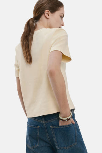 Geel T-shirt met korte mouwen van MANGO, gezien van achter met een paardenstaart en blauwe jeans.
