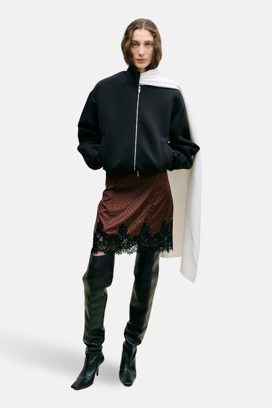 Jupe courte marron de MANGO, à pois noirs et bordure en dentelle, combinée avec un blouson bomber noir et de hautes bottes noires.