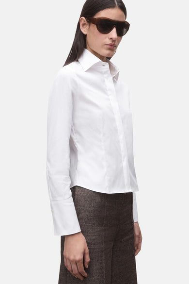 Chemise blanche à manches longues de MANGO, vue de dos, associée à un pantalon marron et des lunettes de soleil.