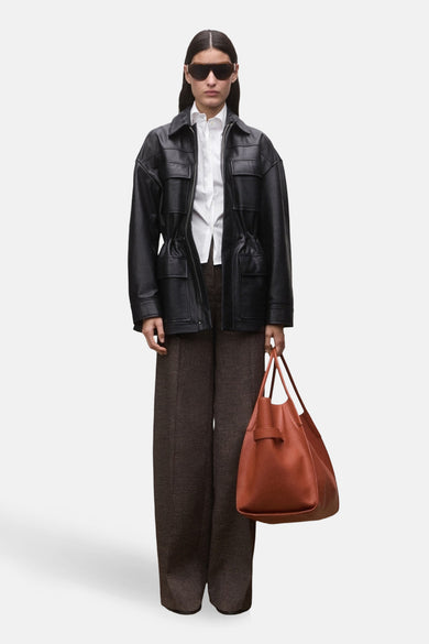 Chemise blanche à manches longues de MANGO, portée sous une veste en cuir noire avec un pantalon et un sac marron.