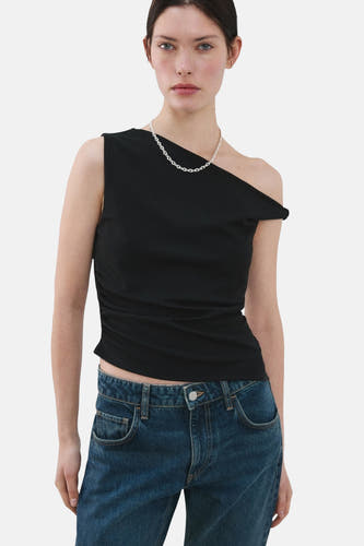 Haut noire sans manches de MANGO, avec une encolure asymétrique et portée avec une chaîne argentée et un jean bleu.