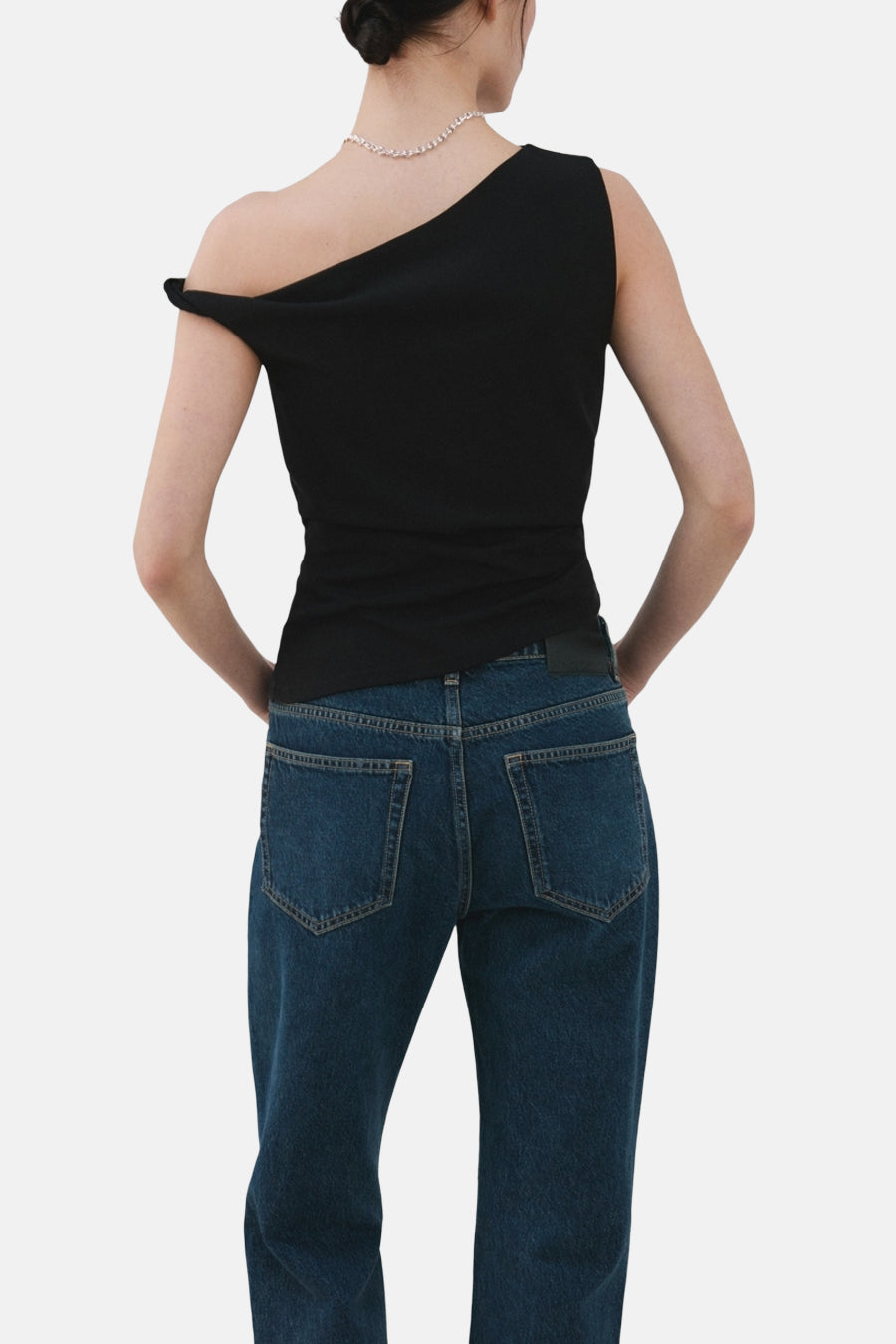Zwarte top zonder mouwen van MANGO, met een asymmetrische halslijn en gedragen met een zilveren ketting en blauwe jeans.