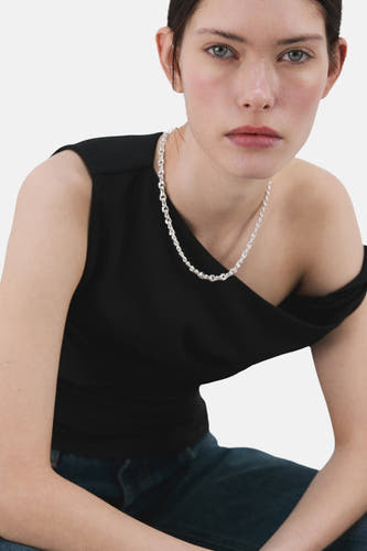 Haut noire sans manches de MANGO, avec une encolure asymétrique et portée avec une chaîne argentée et un jean.