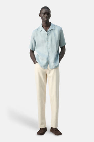 Chemise bleue à manches courtes de MANGO, avec fermeture boutonnée et portée avec un jean clair et des chaussures marron.