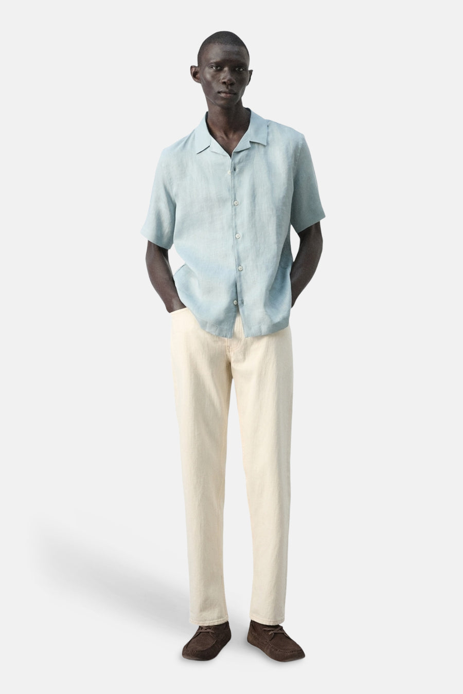 Chemise bleue à manches courtes de MANGO, avec fermeture boutonnée et portée avec un jean clair et des chaussures marron.