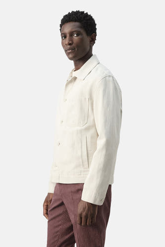 Veste courte écru de MANGO, à manches longues et poches plaquées, portée avec un pantalon rayé.