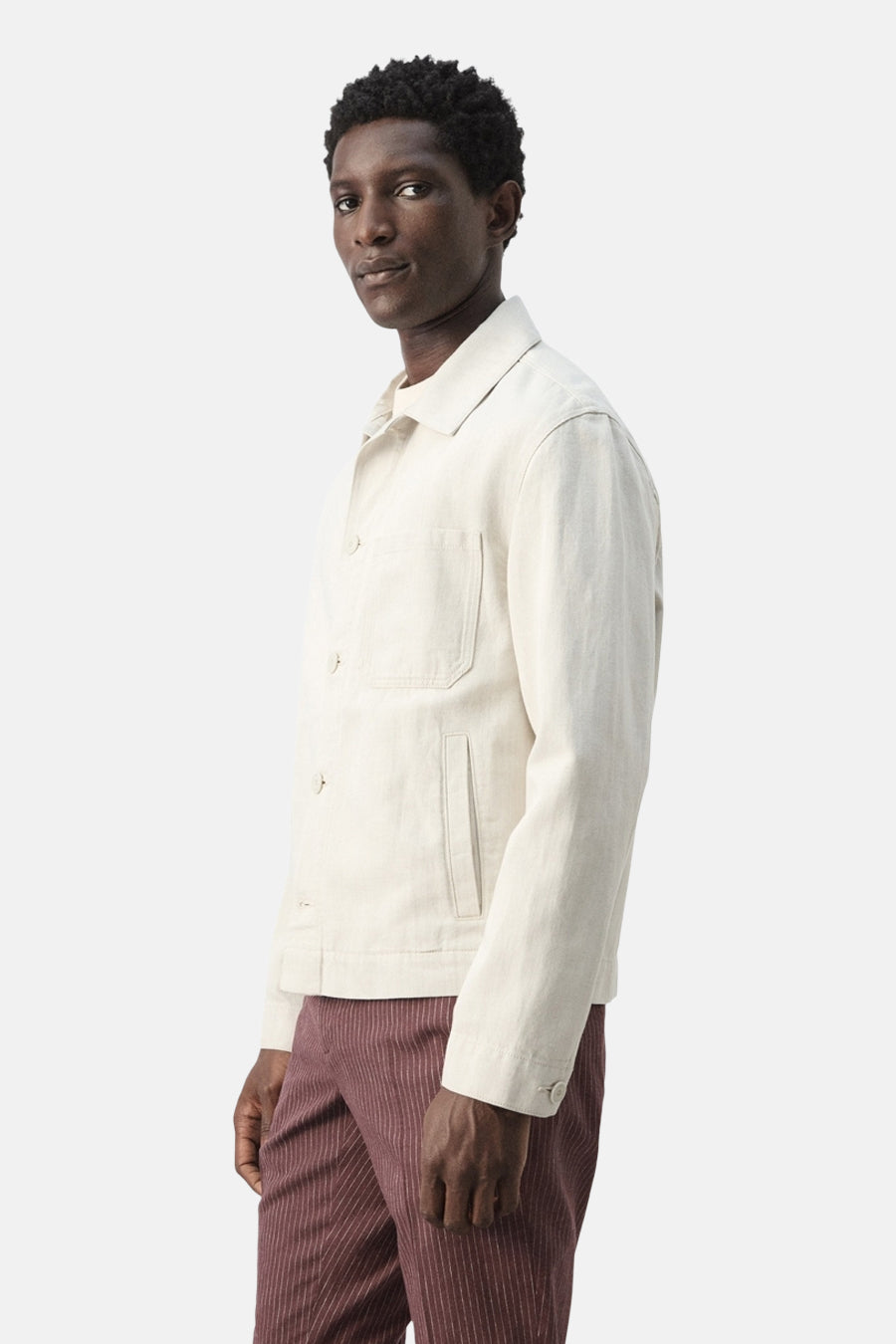 Veste courte écru de MANGO, à manches longues et poches plaquées, portée avec un pantalon rayé.