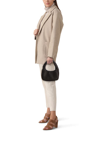 Sac à bandoulière tressé noir de MANGO, en forme de demi-lune, tenu par un mannequin portant un blazer beige et un pantalon crème.