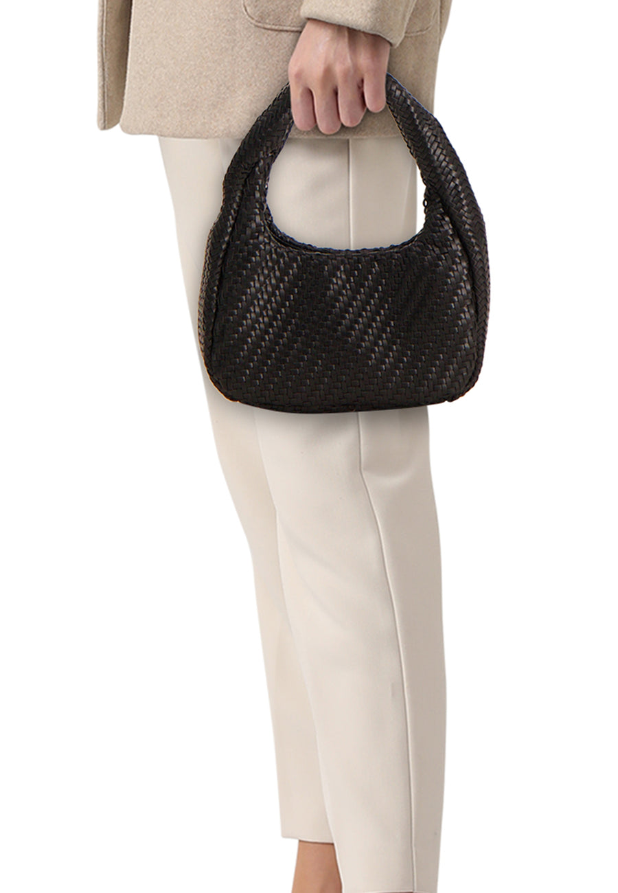 Sac à bandoulière noir de MANGO avec texture tressée, tenu par une personne portant une veste beige et un pantalon crème.