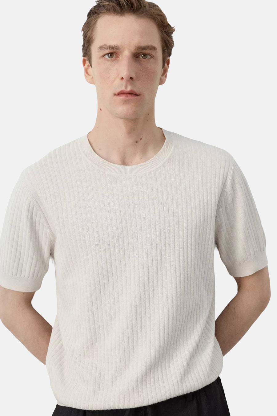 T-shirt écru à manches courtes de MANGO, avec texture côtelée et col rond, porté sur un pantalon noir.
