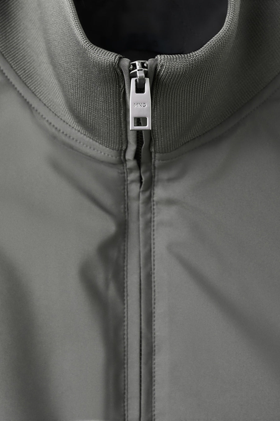 Gilet gris de MANGO, avec une texture lisse et une fermeture éclair argentée à l'avant.