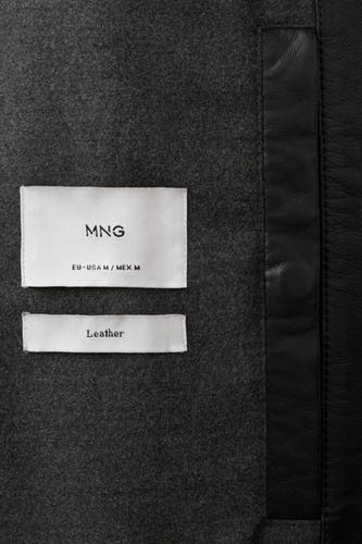 Manteau court noir de MANGO, avec un étiquette portant l'écriture "Leather" et des accents en cuir le long du bord.