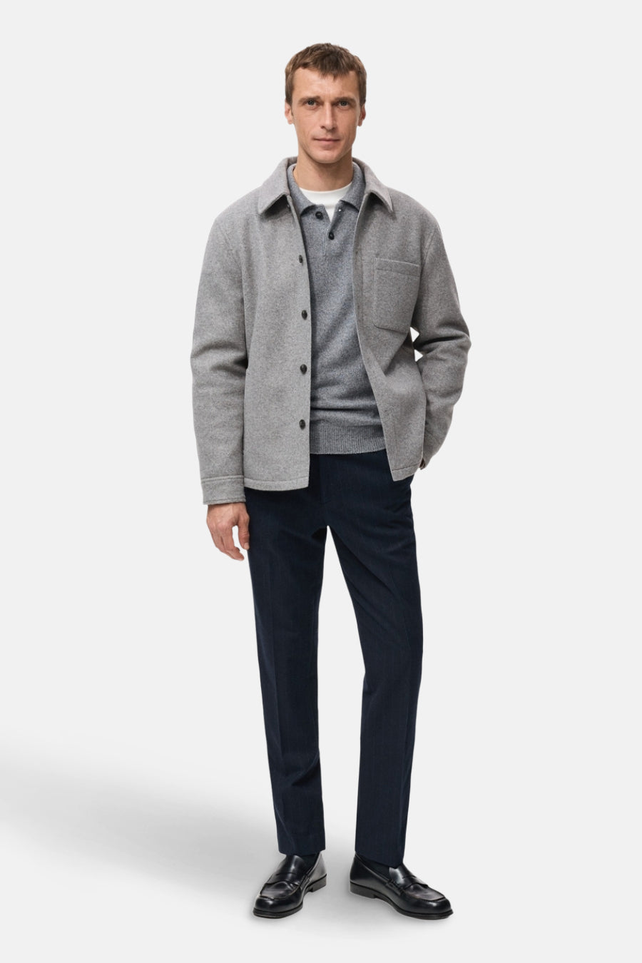 Manteau court gris de MANGO, à boutons, porté sur un polo gris et un pantalon bleu marine avec des loafers.
