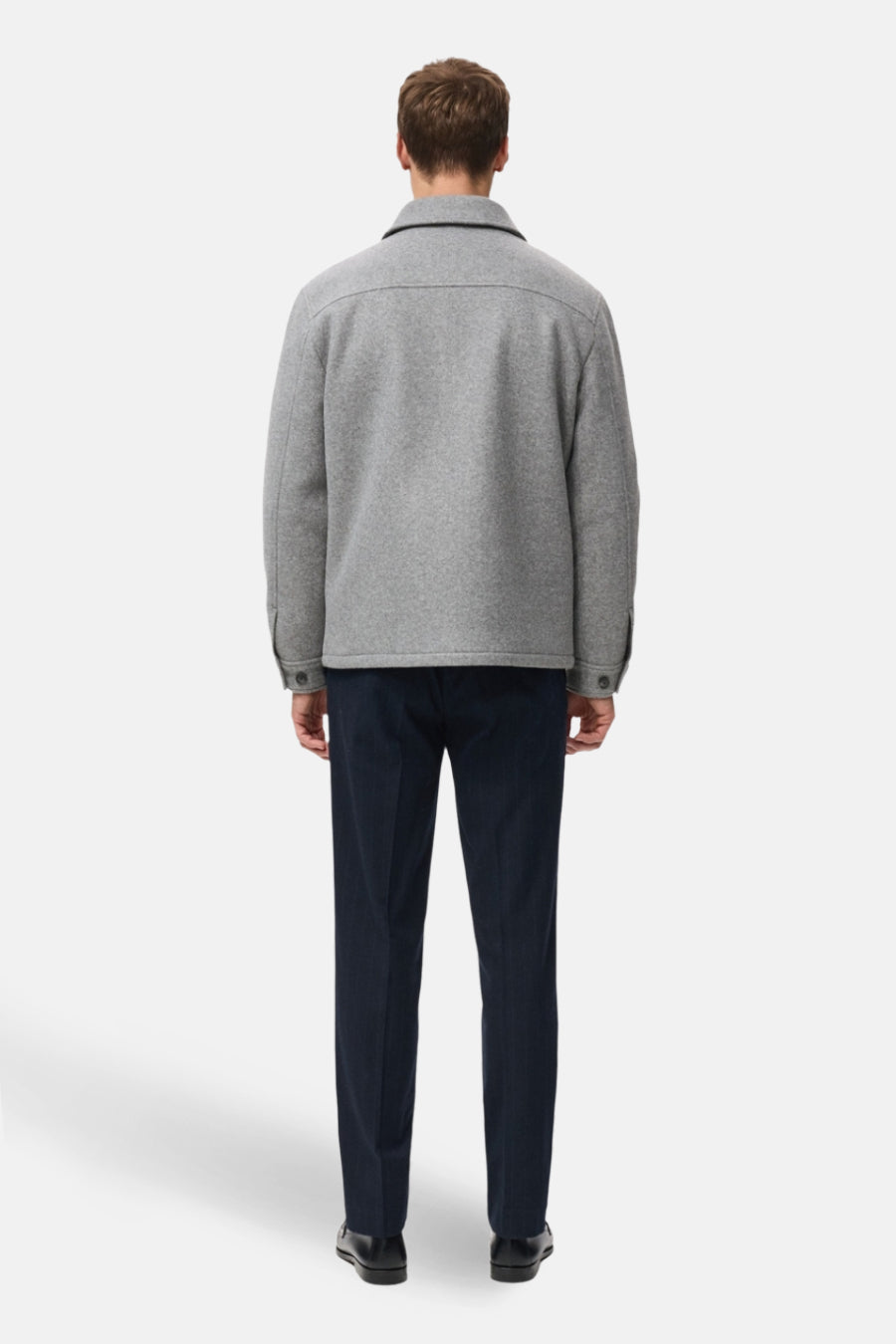 Grijze korte jas van MANGO, achterkant gezien, met donkere pantalon en zwarte schoenen.