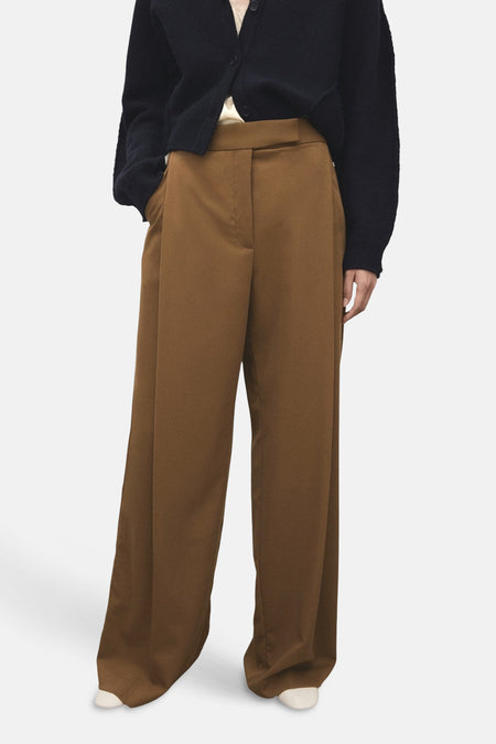 Kakikleurige broek van MANGO, met wijde pijpen en een hoge taille, gedragen met een donkerblauw vest.
