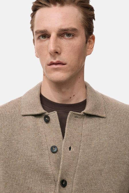 Een man in een beige gebreid vest met bruin shirt.
