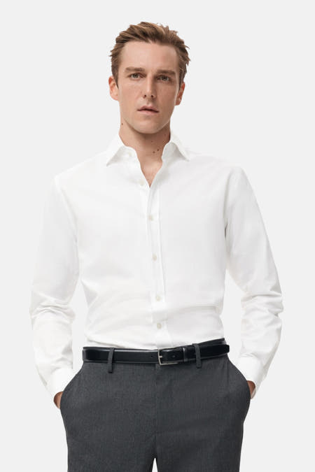 Chemise blanche à manches longues de MANGO, dos visible avec un pantalon gris et une ceinture noire.