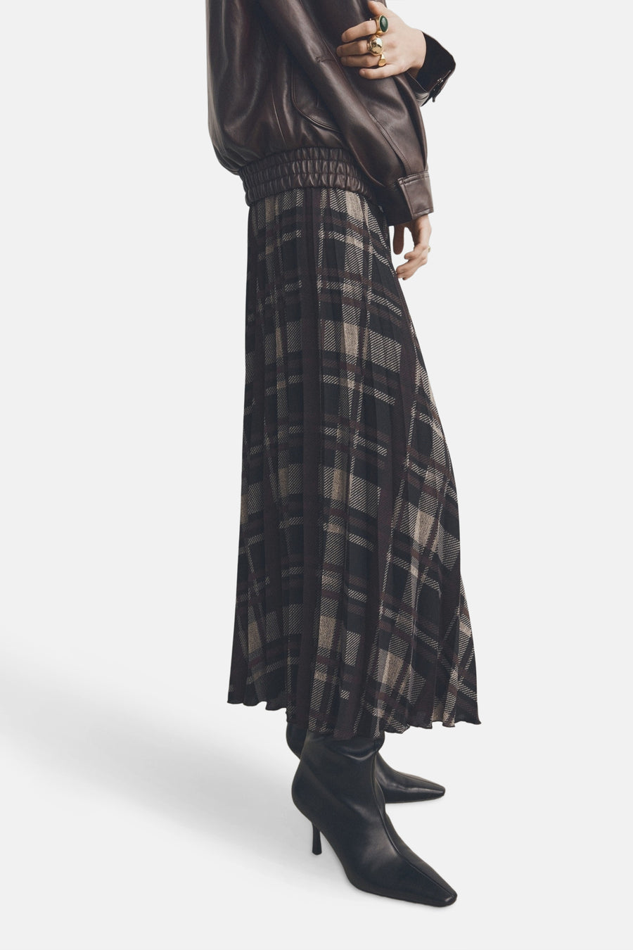 Long jupe multicolore de MANGO, avec une imprimé rayé, texture pliée, associée à un manteau en cuir brun et des bottes noires.