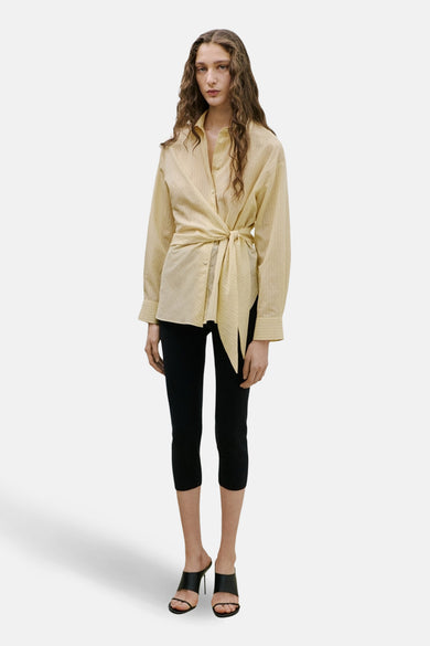 Chemise jaune à manches longues de MANGO, nouée sur le devant, associée à un pantalon noir et des talons.
