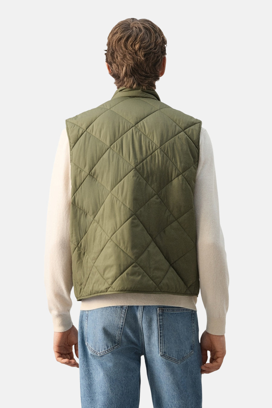 Gilet vert de MANGO avec surpiqûres à carreaux, porté sur un pull de couleur crème et un jean bleu, vue de dos.