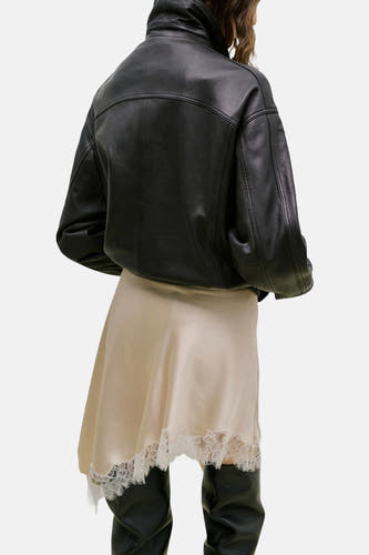Jupe courte beige de MANGO, avec bordure en dentelle et portée avec une veste en cuir noire et des bottes hautes.