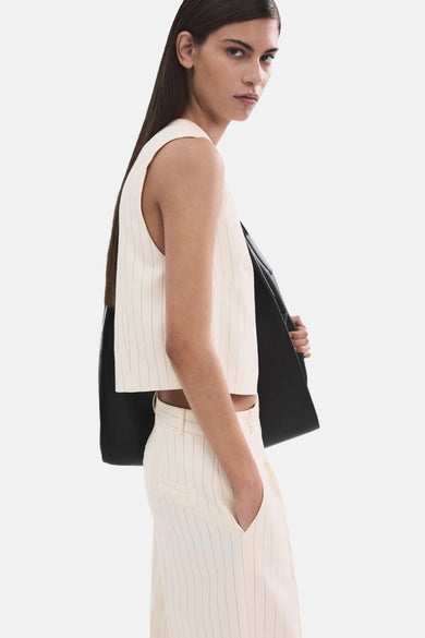 Blouse écru sans manches de MANGO, à rayures craie et avec une veste noire négligemment jetée sur l'épaule.