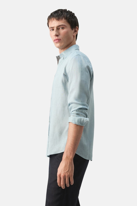 Chemise bleue à manches longues de MANGO, vue de côté avec manches retroussées et un pantalon foncé.