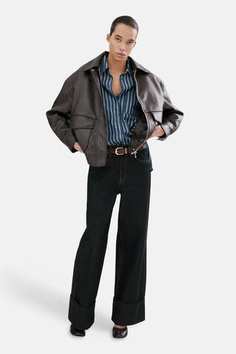 Chemise en jean bleu foncé de MANGO, à rayures verticales et associée à une veste en cuir marron et un jean foncé retroussé.