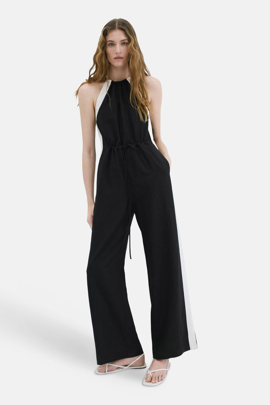 Combinaison noir et blanc de MANGO avec col licou, cordon de serrage à la taille et jambes larges, portée par un mannequin assis.
