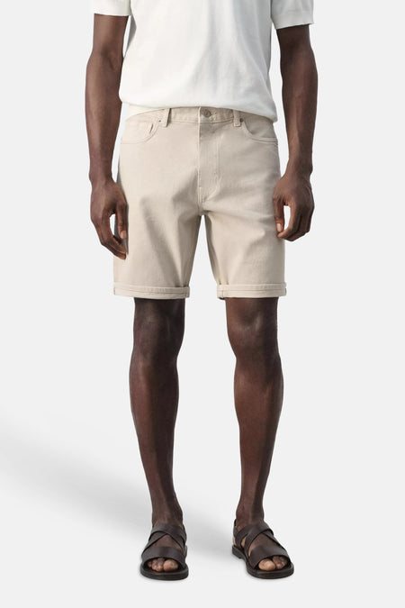 Bermuda beige de MANGO, vue de dos, avec ourlets retroussés et poches arrière, portée avec un t-shirt blanc et des sandales.