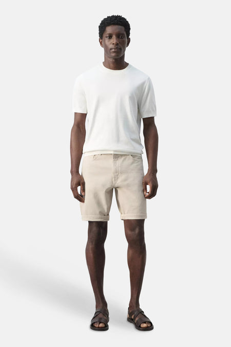 Bermuda beige de MANGO, avec ourlets retroussés, porté par un homme avec un T-shirt blanc et des sandales marron foncé.