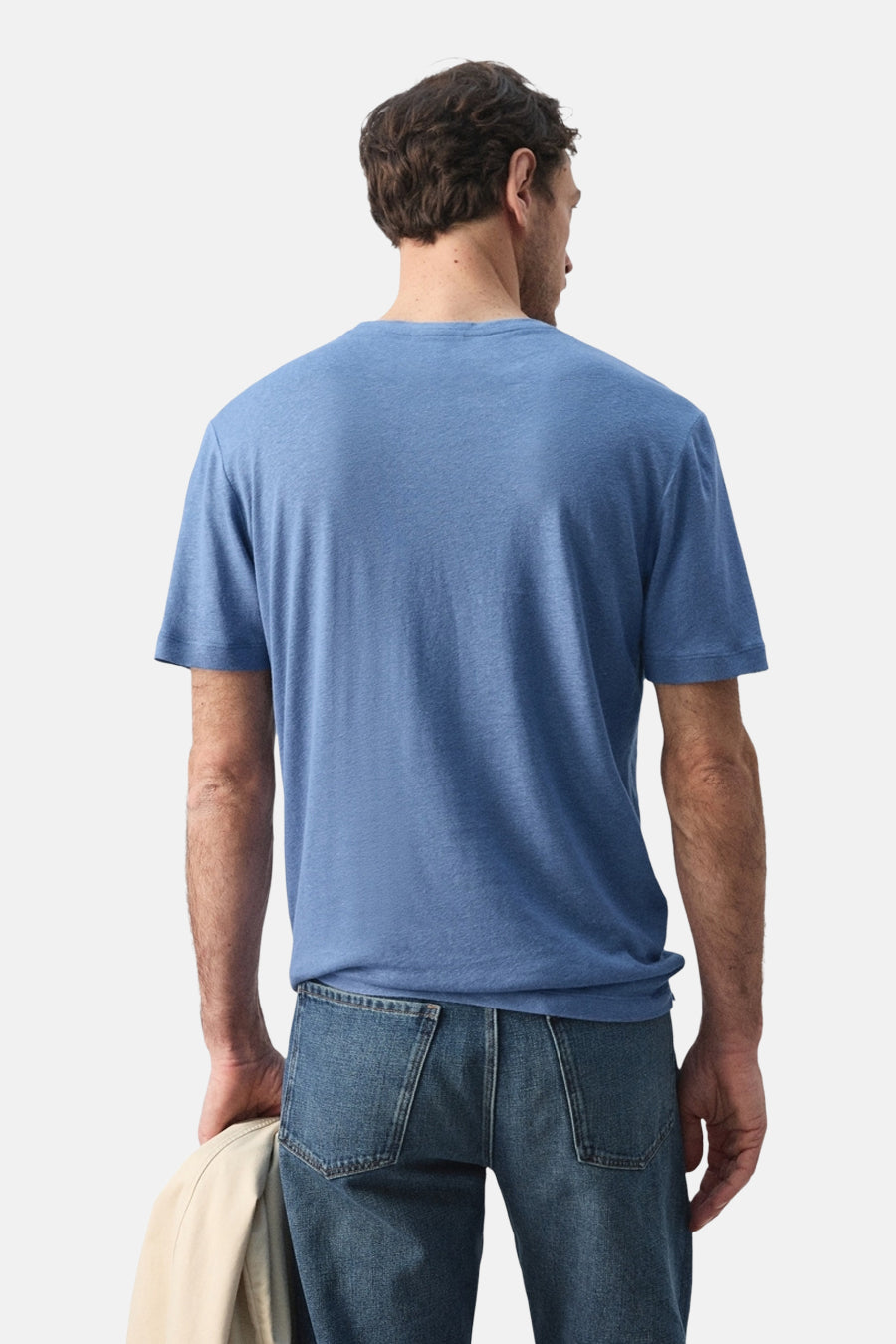 Blauw T-shirt met korte mouwen van MANGO, gezien van achteren, met jeans en een jas in de hand.
