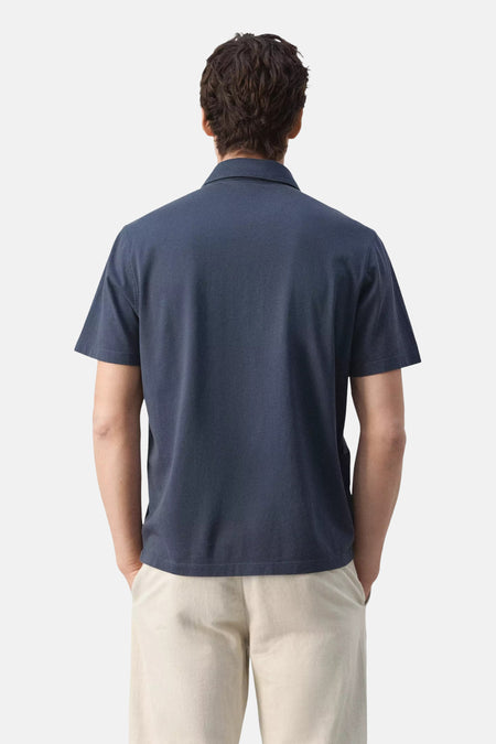 Blauwe polo van MANGO met korte mouwen, gedragen door een man in lichte broek, rugaanzicht.