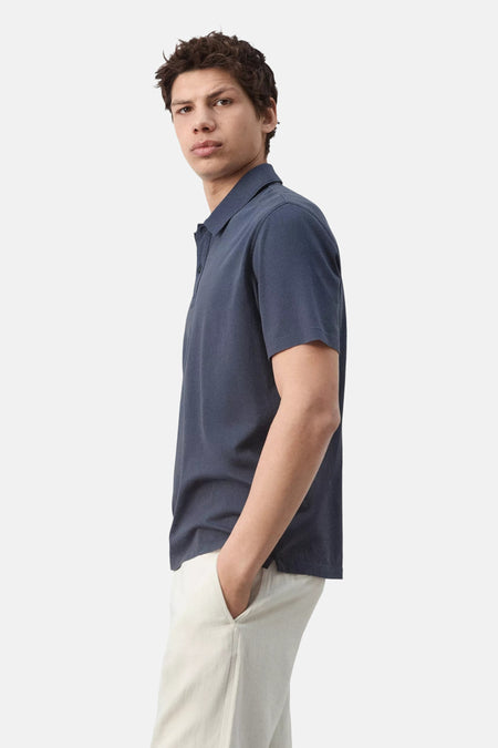 Polo bleue de MANGO à manches courtes et col, portée par un homme avec la main dans la poche, vue de profil.