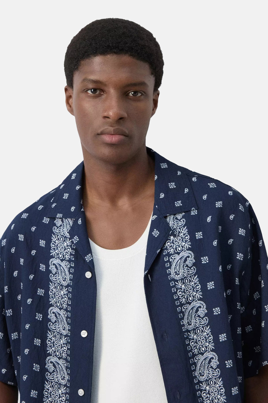 Chemise bleue à manches courtes de MANGO, avec des motifs cachemire et géométriques blancs, portée sur un débardeur blanc.