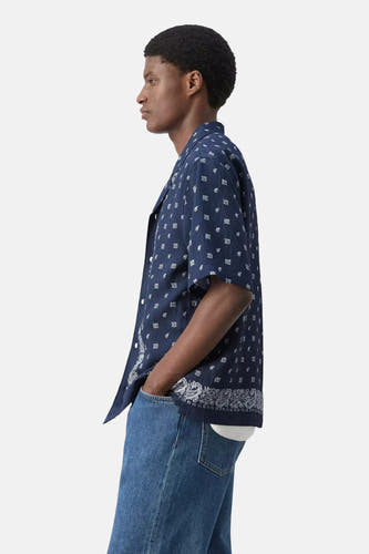 Chemise bleue à manches courtes de MANGO avec motif bandana blanc, portée par un homme en jean, de profil.