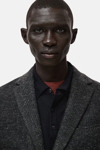 Blazer multicolore de MANGO, avec un motif subtil et une fine texture, porté sur un chemisier sombre avec une collette rouge.