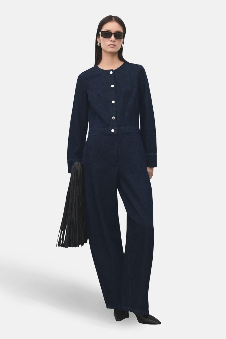 Combinaison de denim bleu marine de MANGO, avec des manches longues, une fermeture à boutons et des poches, associée à des chaussures noires.