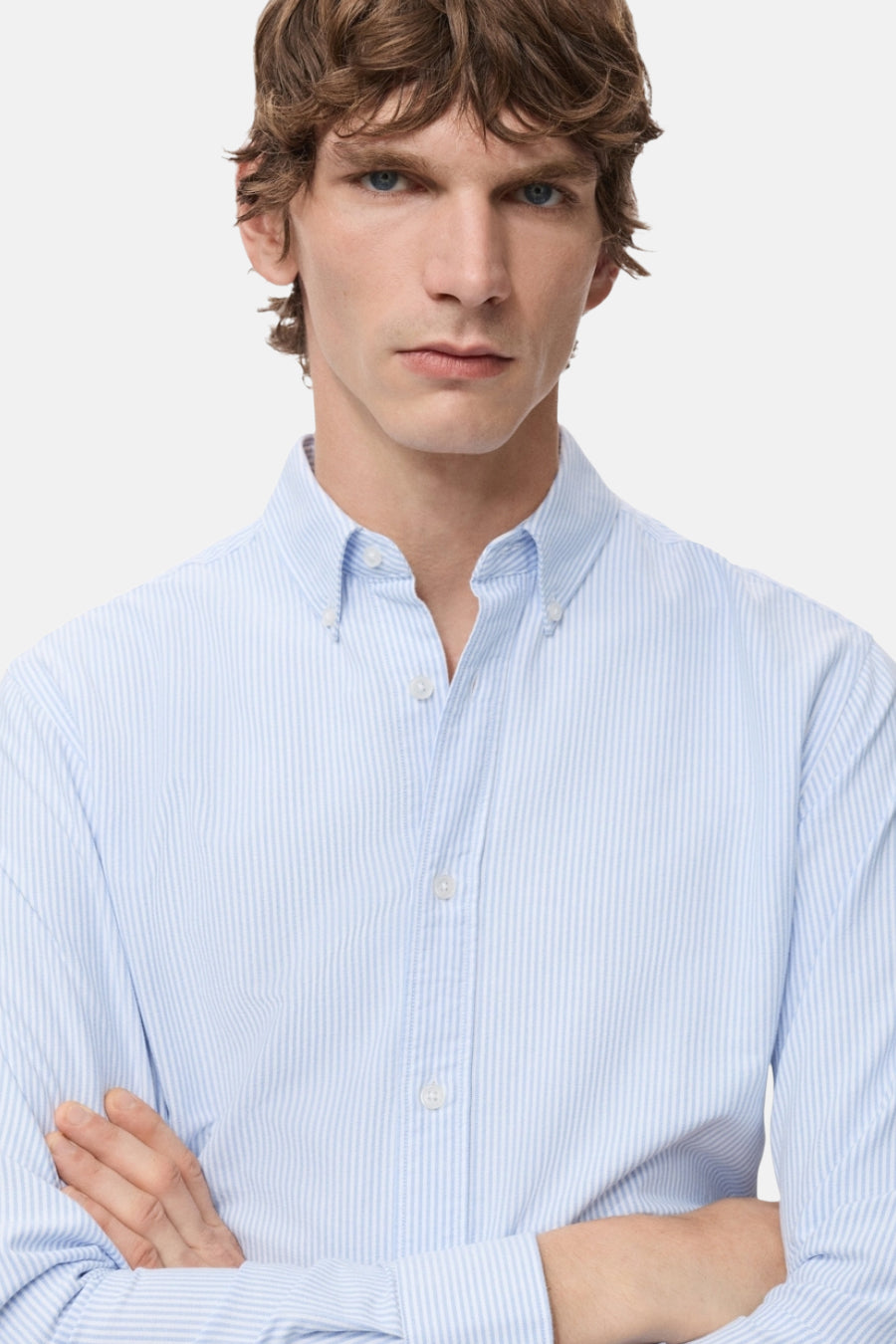Een man in een blauw gestreept overhemd met lange mouwen en gekruiste armen.
