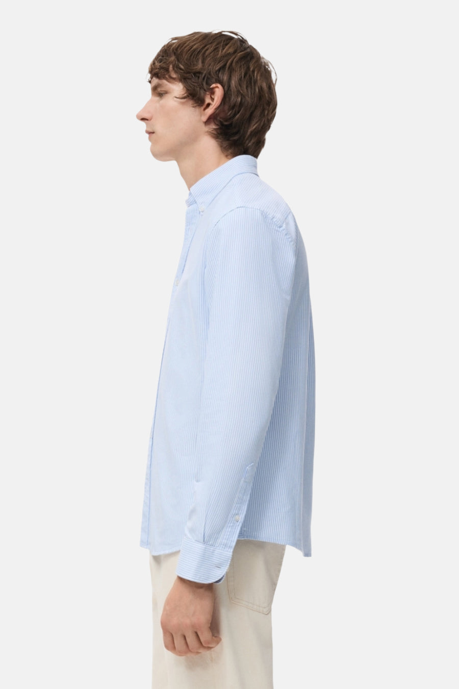 Man in gestreept lichtblauw overhemd, zijprofiel, witte achtergrond.
