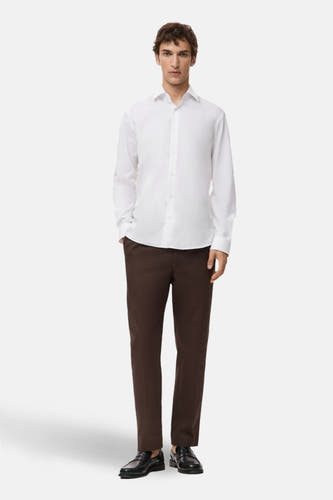 Blouse blanche à manches longues de MANGO, associée à un pantalon marron et des chaussures noires.