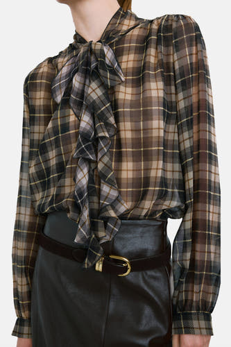 Blouse multicolore à longues manches de MANGO, avec un motif à carreaux, portée avec une jupe noire fendue et des chaussures marron.