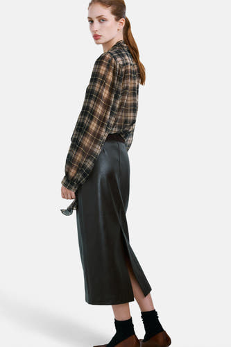 Multikleurige blouse met lange mouwen van MANGO, met ruitpatroon, gedragen met een zwarte rok met split en bruine schoenen.
