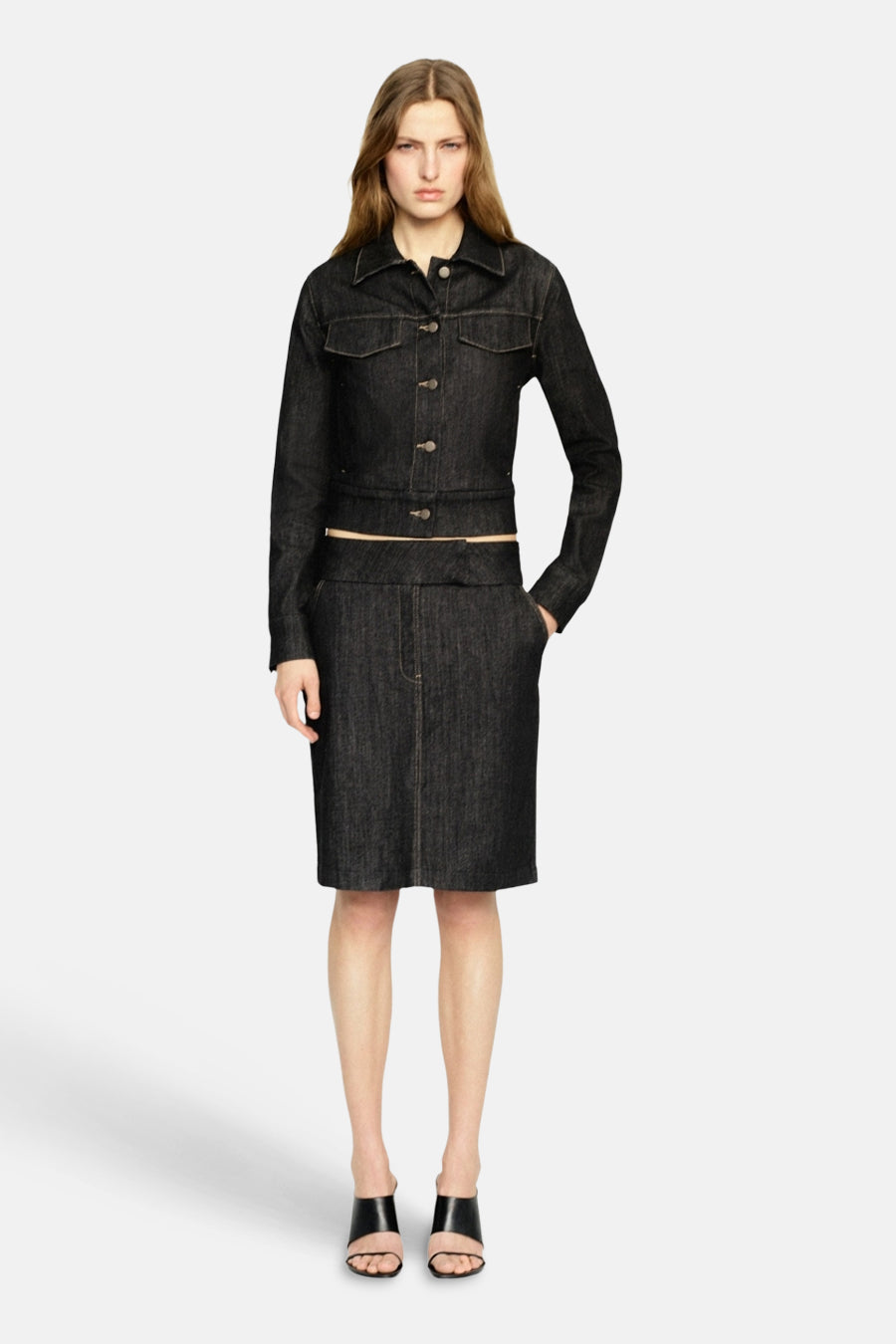 Veste en jean bleu foncé de MANGO, à manches longues et fermeture boutonnée, associée à une jupe assortie et des sandales noires.