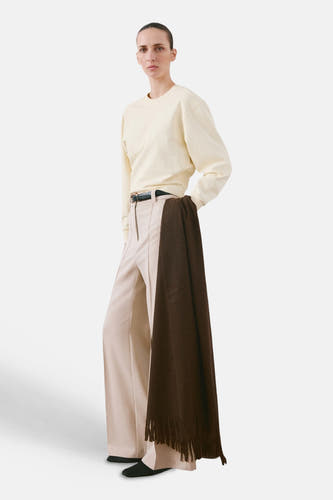 Pull beige de MANGO, à manches longues, porté avec un pantalon ample et une écharpe marron.