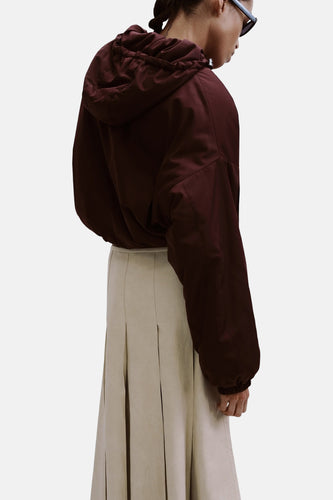 Lange beige rok van MANGO, met plooien en een lichte textuur, gecombineerd met een bordeauxrode jas met capuchon.