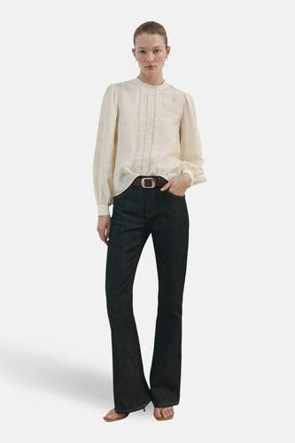 Blouse écru (manches longues) de MANGO, avec détails brodés le long du col et des manches, combinée avec un jean et une ceinture marron.